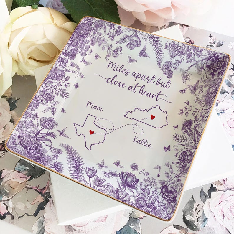 May include: Square ceramic dish with a floral and butterfly design in purple and gold. The dish has the text "Miles apart but close at heart" with a map of Texas and Kentucky, and the names "Mom" and "Kallie".
