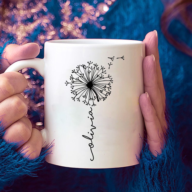 May include: White ceramic mug with a black dandelion design and the name "Olivia" written vertically below the dandelion.