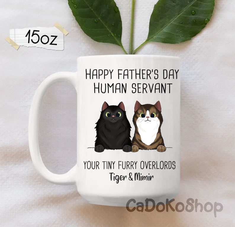 May include: White ceramic mug with a black and brown cat illustration. The mug reads "Happy Father's Day Human Servant Your Tiny Furry Overlords Tiger & Mimir".