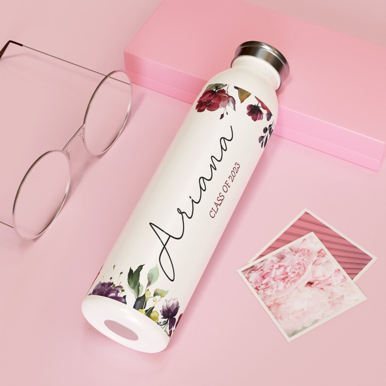 May include: White water bottle with a floral design and the name "Ariana" and the text "Class of 2023" printed on it.