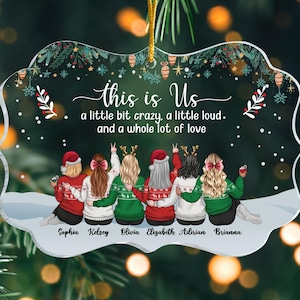 May include: A clear acrylic Christmas ornament with a festive design. The ornament features six figures in sweaters, with the text "this is Us" and the phrase "a little bit crazy, a little loud, and a whole lot of love." Names are printed below the figures.