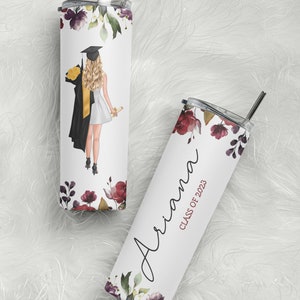 May include: Two stainless steel tumblers with a floral design. One tumbler has a graduation cap and gown illustration and the other has the name "Ariana" and the text "Class of 2023".