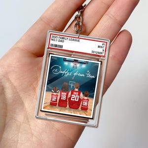 May include: A clear acrylic keychain featuring a basketball-themed family portrait. The image shows a family of four in red jerseys with the text "Daddy's dream team." The keychain also has the text "2025 Family League No. 1 Dad."
