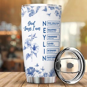 Może przedstawiać: Biały kubek ze stali nierdzewnej z niebieskim kwiatowym wzorem i napisem "Bóg mówi, że jestem". Kubek zawiera również słowa "NEYLIN" z powiązanymi wersetami biblijnymi. Pokrywka jest srebrna i częściowo otwarta.