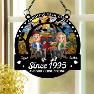 May include: Black metal sign with a chain for hanging. The sign features a couple sitting in chairs, a red truck, and the text "ANNOYING EACH OTHER" and "Since 1995 AND STILL GOING STRONG". The background shows a sunset and a house.