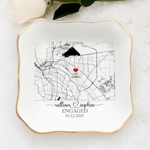 May include: A white ceramic ring dish with a gold rim features a black and white map design. The map includes a heart marking a location labeled "LAST CHANCE." The dish is personalized with names and the date "10.12.2025" and the word "ENGAGED."