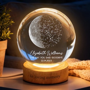 Peut inclure: Une sphère en verre transparent avec un motif détaillé de lune et de constellations, posée sur une base en bois. La sphère porte l'inscription "Elizabeth Williams", la phrase "THE DAY YOU SAID GOODBYE" et la date "12.04.2023". La base indique "In loving memory".