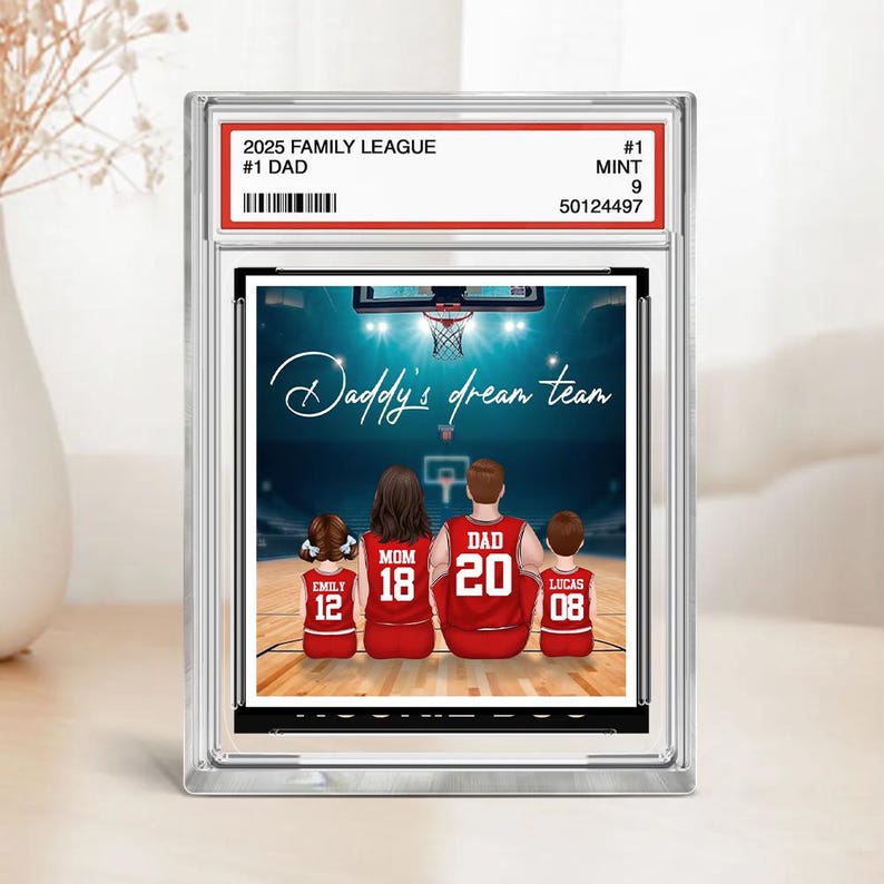 May include: A framed print featuring a basketball court scene with a family of four wearing red jerseys. The text "Daddy's dream team" is displayed above the family. The frame includes the text "2025 Family League #1 Dad".