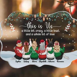 May include: Clear acrylic ornament with a festive design. The ornament features six figures wearing sweaters and Santa hats, with the text "this is Us" and the names Sophia, Kelsey, Olivia, Elizabeth, Adirian, and Brianna.