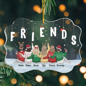 May include: A clear, decorative ornament with the word "FRIENDS" in white letters. The ornament features a group of friends wearing holiday sweaters and hats, with their names below. A gold string is attached for hanging.