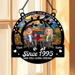 May include: A black metal sign with the text "ANNOYING EACH OTHER." It features a couple sitting in chairs, a red truck, and the text "Since 1995 AND STILL GOING STRONG." The names "Elijah" and "Sophia" are also included. The sign has a decorative border.