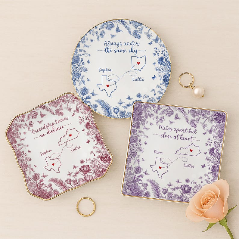 May include: Three decorative ceramic plates with floral designs and gold rims. Each plate features a map outline with connecting lines and text: "Always under the same sky," "Friendship knows no distance," and "Miles apart but close at heart."