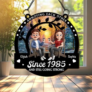 May include: A black decorative sign with the text "ANNOYING EACH OTHER" and "Since 1985 AND STILL GOING STRONG." The sign features a cartoon couple holding coffee cups, sitting in chairs, with a winter forest scene in the background.