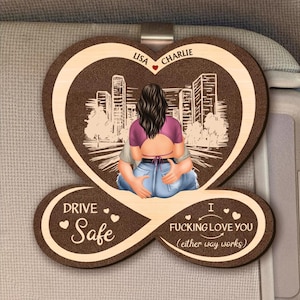 May include: A wooden car visor clip in the shape of a heart with a couple embracing, and city skyline in the background. The names "Lisa" and "Charlie" are above the couple. The text "Drive Safe" and "I Fucking Love You (either way works)" are also included.