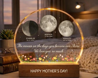 May include: A personalized Mother's Day gift featuring three moon phases with names and dates. The clear acrylic panel has the text "The moons on the days you became our Mom, We love you so much." The wooden base reads "HAPPY MOTHER'S DAY!"