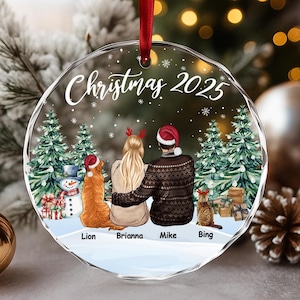 Peut inclure: Ornement de Noël rond et transparent avec un ruban rouge. L'ornement présente une scène familiale avec un couple, deux animaux de compagnie et le texte "Christmas 2025". La famille est entourée d'arbres de Noël et de neige.