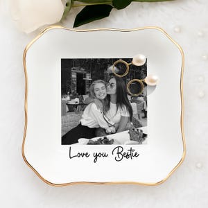 May include: White ceramic trinket dish with a gold rim and a black and white photo of two people. The dish has the words "Love you Bestie" in a handwritten font.