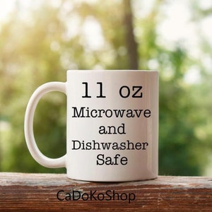 K&ouml;nnte beinhalten: Wei&szlig;e Keramiktasse mit schwarzem Text, der "11 oz Mikrowelle und Sp&uuml;lmaschinenfest" lautet.
