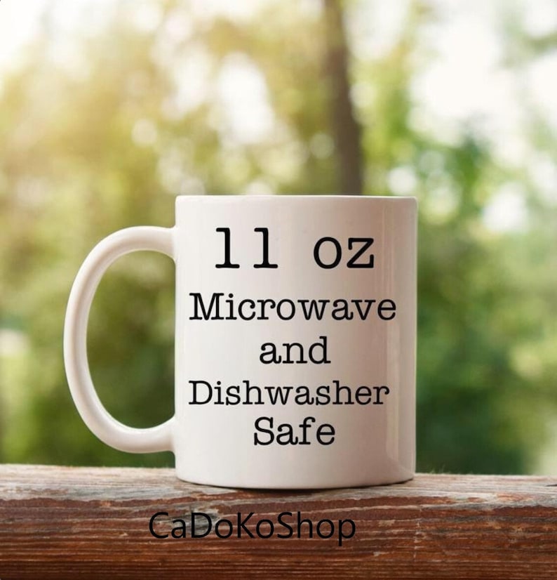 K&ouml;nnte beinhalten: Wei&szlig;e Keramiktasse mit schwarzem Text, der "11 oz Mikrowelle und Sp&uuml;lmaschinenfest" lautet.
