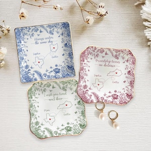 May include: Three decorative ceramic dishes with floral patterns and gold rims. Each dish features a state map with names and the phrases: "Always under the same sky", "Friendship knows no distance", and "I wish you lived next door".