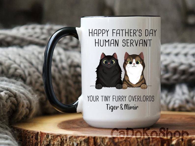 May include: White ceramic coffee mug with a black handle. The mug has a black rim and features a funny message that reads "Happy Father's Day Human Servant Your Tiny Furry Overlords Tiger & Mimir". The mug has a cartoon image of two cats.