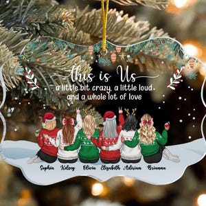 May include: A clear acrylic Christmas ornament with a gold string for hanging. The ornament features six figures in sweaters, with the text "this is Us" and the names Sophia, Kelsey, Olivia, Elizabeth, Adirian, and Brianna.