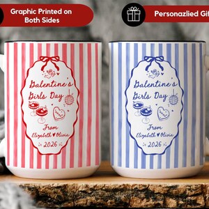 May include: Two ceramic mugs with black handles. One mug is red and white striped, the other is blue and white striped. Both mugs have a Valentine's Girls Day design with text and illustrations. The text reads "Dalentine's Girls Day" and "From Elizabeth & Olivia 2026".