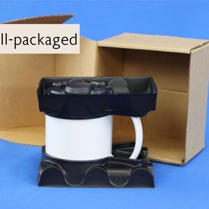 Puede incluir: Una taza de cer&aacute;mica blanca con asa negra est&aacute; empaquetada en una caja de cart&oacute;n con un inserto de espuma negra. La caja est&aacute; abierta y la taza es visible en el interior. El texto "Bien empaquetado" es visible en la esquina superior izquierda de la imagen.