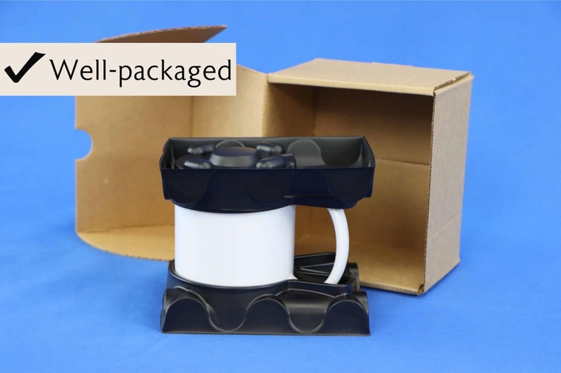 Puede incluir: Una taza de cer&aacute;mica blanca con asa negra est&aacute; empaquetada en una caja de cart&oacute;n con un inserto de espuma negra. La caja est&aacute; abierta y la taza es visible en el interior. El texto "Bien empaquetado" es visible en la esquina superior izquierda de la imagen.