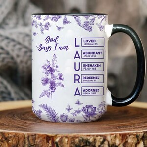Pu&ograve; includere: Tazza in ceramica bianca con manico e bordo neri, con il nome "LAURA" in lettere viola. La tazza &egrave; decorata con motivi floreali e farfalle e il testo "Dio dice che io sono" e versetti biblici.