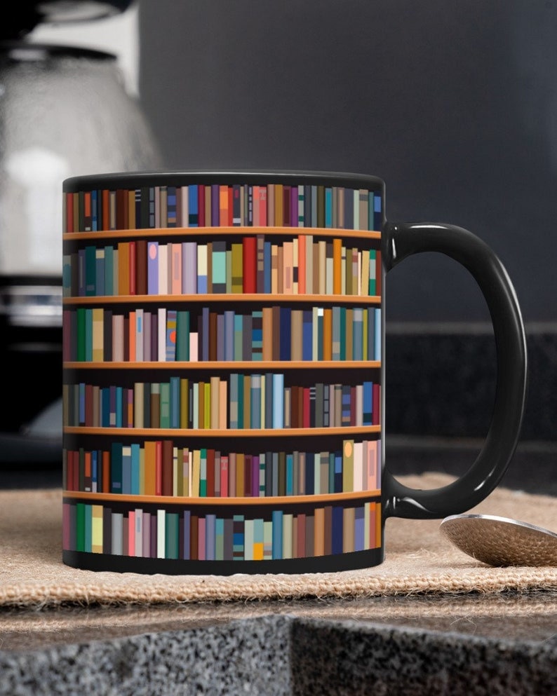 Op de afbeelding: Zwarte koffiemok met een boekenkastontwerp met kleurrijke boeken in de planken. De mok heeft een zwart handvat.