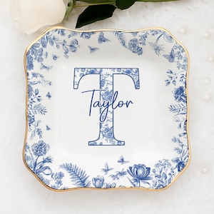 May include: A white, square decorative tray with a blue floral design and gold trim. The tray features a large blue letter "T" and the name "Taylor" in script. Butterflies and flowers decorate the border.