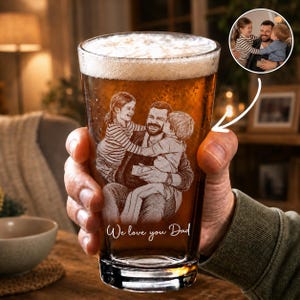 Op de afbeelding: Een pintglas gevuld met bier, vastgehouden door een persoon. Het glas is geëtst met een familieportret en de woorden "We love you Dad". De afbeelding toont een vader die twee kinderen omarmt. Een kleinere afbeelding van de familie staat rechtsboven.