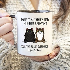 May include: White ceramic mug with a black rim and handle. The mug has a black and brown cat illustration and the text "Happy Father's Day Human Servant Your Tiny Furry Overlords Tiger & Mimir".