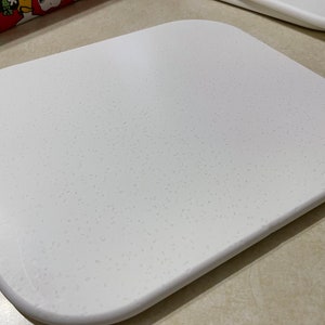 May include: A white, square-shaped cutting board with a textured surface. The board is made of a durable material and is perfect for preparing food.