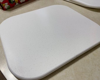 May include: A white, square-shaped cutting board with a textured surface. The board is made of a durable material and is perfect for preparing food.