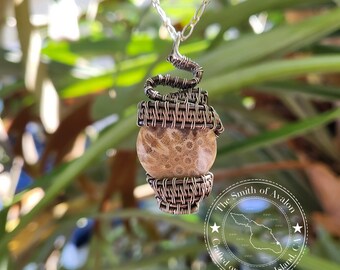 May include: A copper wire wrapped pendant featuring a brown and white stone with a silver chain. The pendant is labeled "The Smith of Avalon Crafted on Catalina Island, CA."