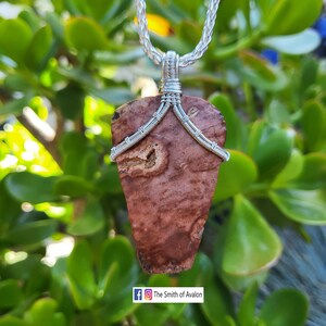 May include: A silver chain necklace with a brown and red stone pendant. The stone is wrapped in silver wire and has a unique, natural pattern. The pendant is shaped like a teardrop.