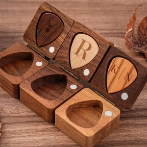 May include: A wooden box with four compartments, each shaped like a guitar pick. The box is open and the compartments are empty. The box is made of dark wood and has a light wood interior. The compartments are labeled with the names "Robin", "R", "KIN", and a deer silhouette.