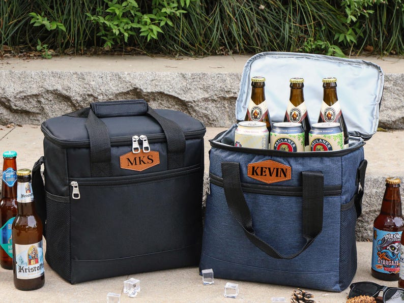 Puede incluir: Dos bolsas isot&eacute;rmicas personalizadas, una negra con el nombre "MKS" y otra azul con el nombre "KEVIN". Ambas bolsas est&aacute;n llenas de botellas y latas de cerveza.