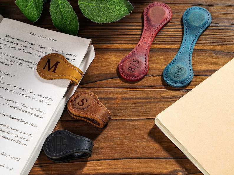 May include: Five leather book markers with different colors and personalized initials. The initials are "M", "S", "RIS", "SNK", and "MAS".