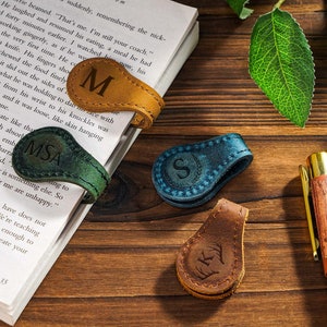 May include: Three leather book markers with personalized initials. The markers are in brown, green, and blue leather. The initials are "M", "MSA", and "S".