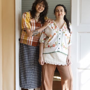 May include: A yellow and brown plaid short-sleeve button-down shirt with a navy blue plaid midi skirt, and a white short-sleeve button-down shirt with colorful floral embroidery paired with tan wide-leg trousers and a white lace hem.