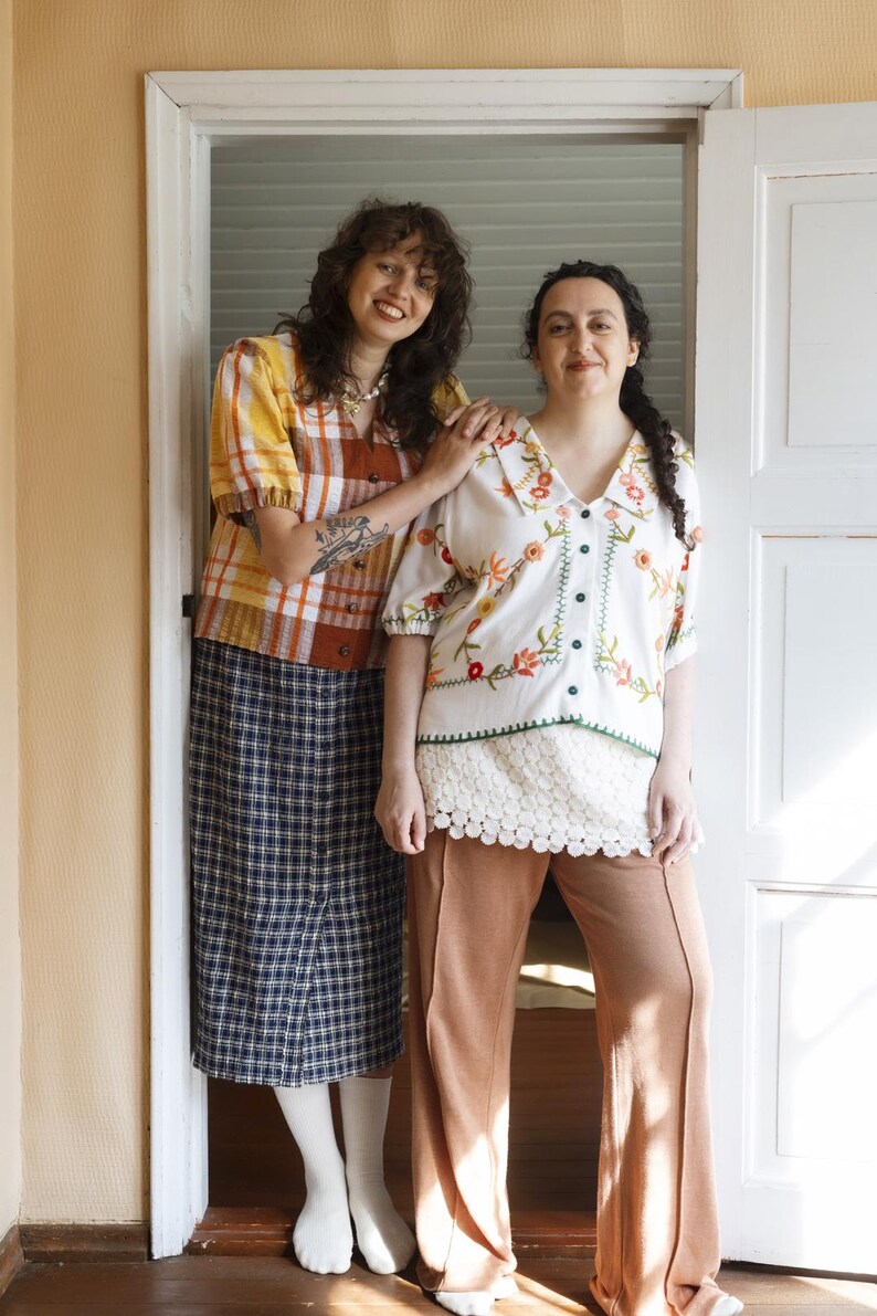 May include: A yellow and brown plaid short-sleeve button-down shirt with a navy blue plaid midi skirt, and a white short-sleeve button-down shirt with colorful floral embroidery paired with tan wide-leg trousers and a white lace hem.