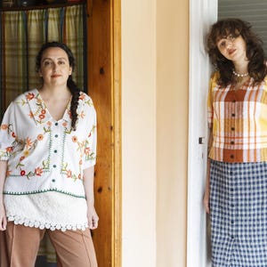 May include: A white blouse with floral embroidery and a button-down front, paired with brown trousers. Beside it, a yellow and orange plaid short-sleeved blouse with a button-down front, worn with a blue and white plaid button-down midi skirt.