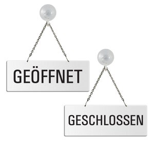 May include: Two silver signs with black text hanging from suction cups. The top sign reads "GEÖFFNET" and the bottom sign reads "GESCHLOSSEN".