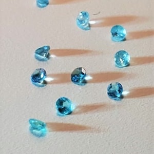 May include: A collection of 15 light blue gemstones scattered on a white surface.
