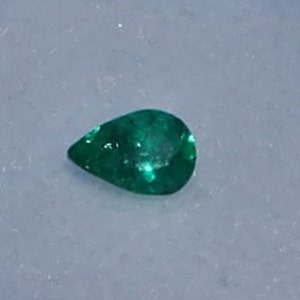 May include: A pear-shaped emerald gemstone with a deep green colour.