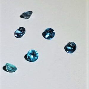May include: Six blue topaz gemstones of various shapes and sizes on a white background.