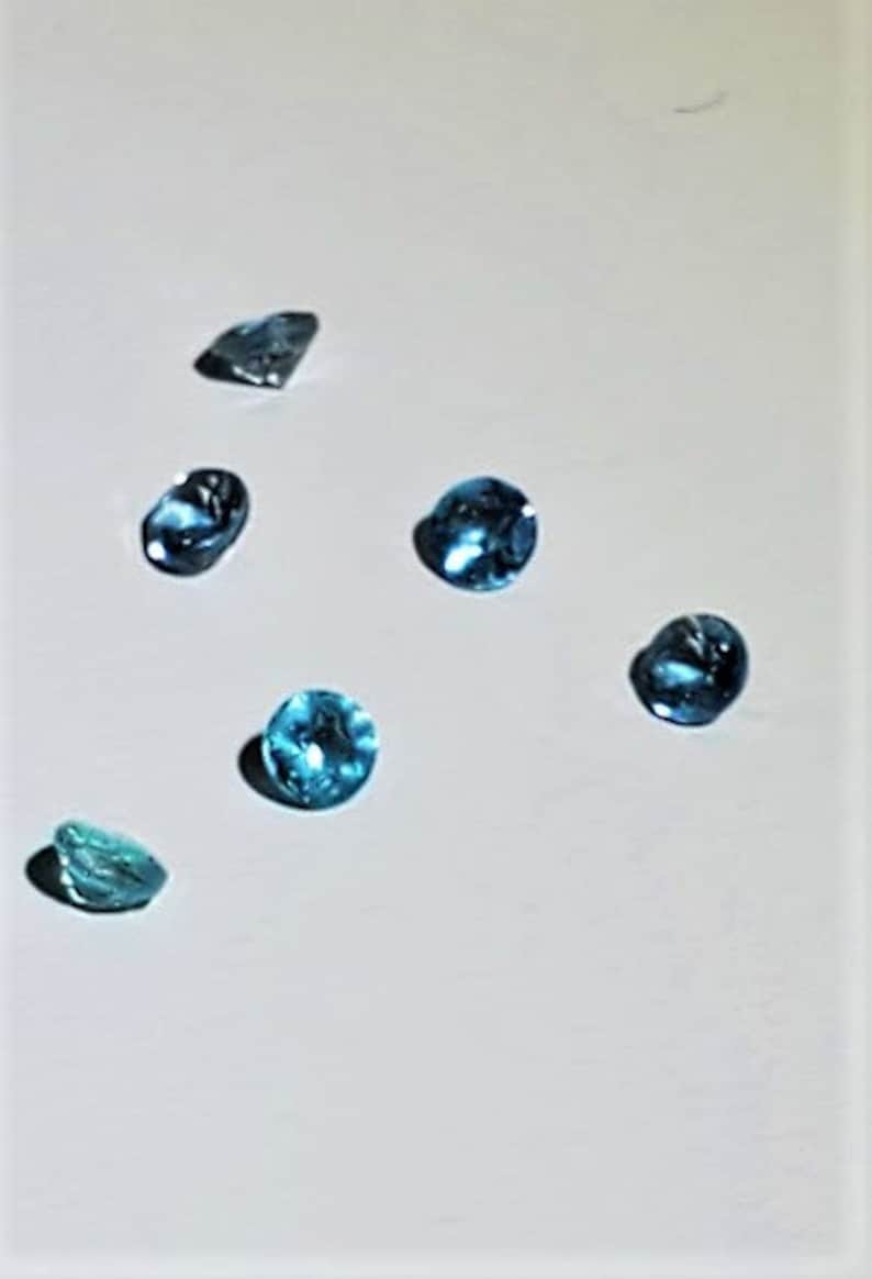 May include: Six blue topaz gemstones of various shapes and sizes on a white background.
